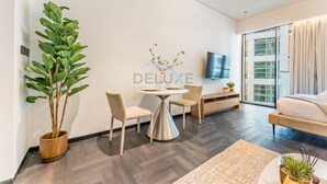 A modern living room with a dining area, a large potted plant, a round table, and a sofa. - Tranquil Studio with City View, O10 Building (Dubai)
