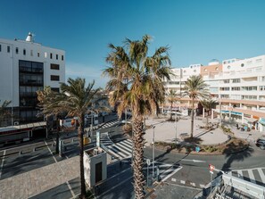 Eine moderne Stadtkreuzung mit Palmen, einer Fußgängerzone und mehrstöckigen Gebäuden mit Geschäftsräumen.