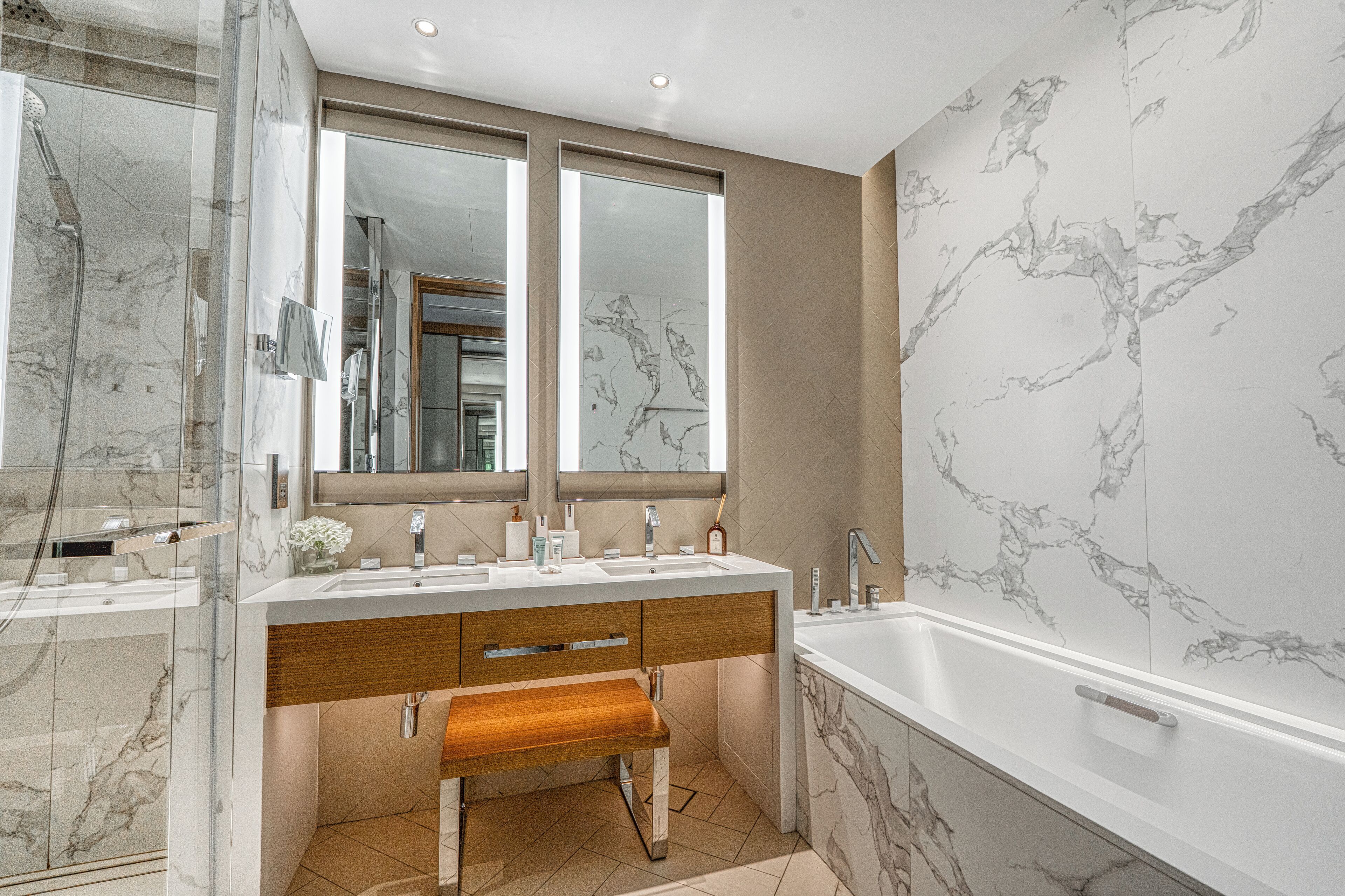 A modern bathroom with a marble vanity, a large mirror, a bathtub, and a shower area.