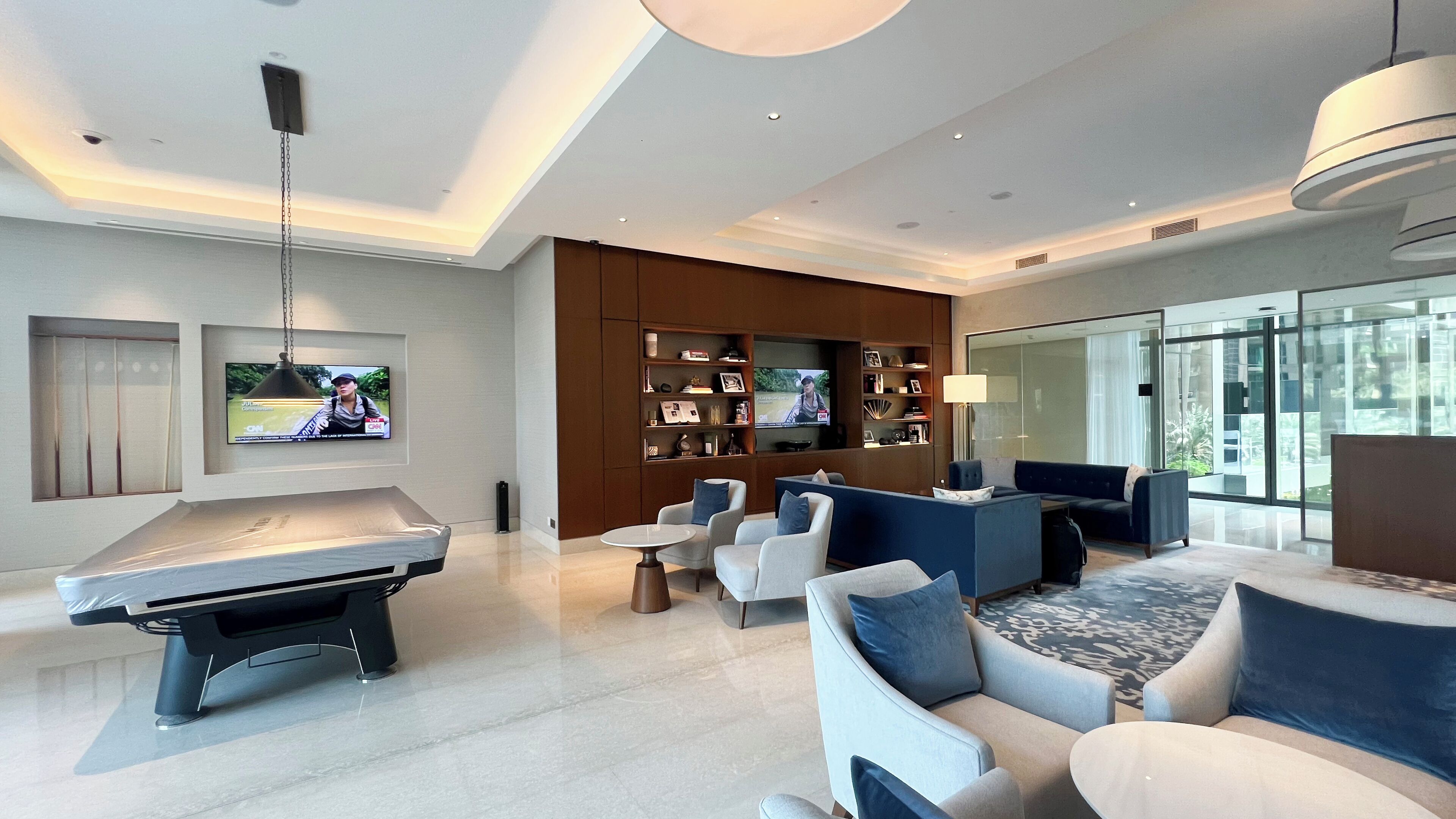 A modern living room with a pool table, comfortable seating, a TV, and a large window offering a view.