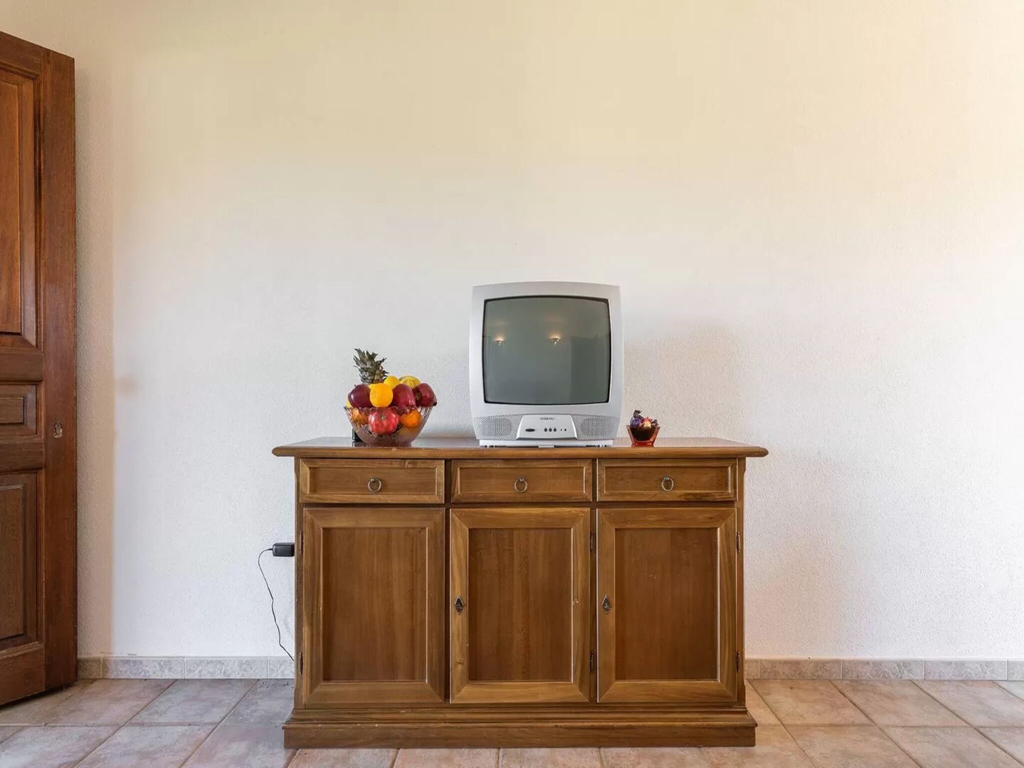 A wooden cabinet with a television on top, a fruit bowl, and a small decorative item.