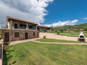 A two-story house with stone walls and a tiled roof, a paved driveway, and a grassy lawn. - Relaxing Home Near the sea (Siniscola)