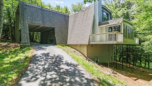 Un edificio moderno con una zona esterna coperta, un vialetto che vi conduce e uno sfondo boscoso.