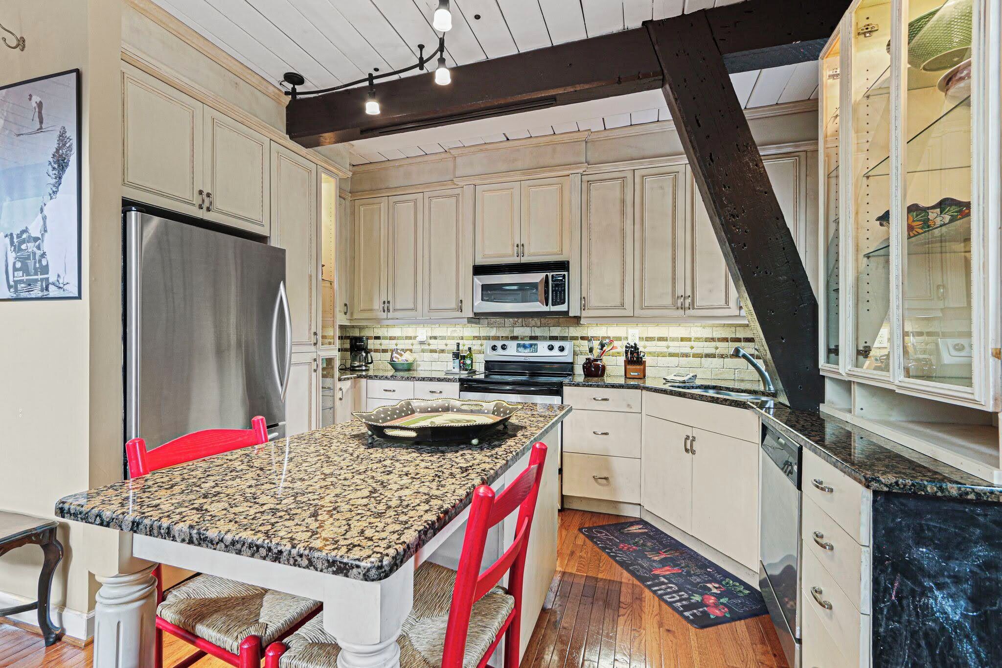 A kitchen with white cabinets, a stainless steel refrigerator, a microwave, and a granite countertop.