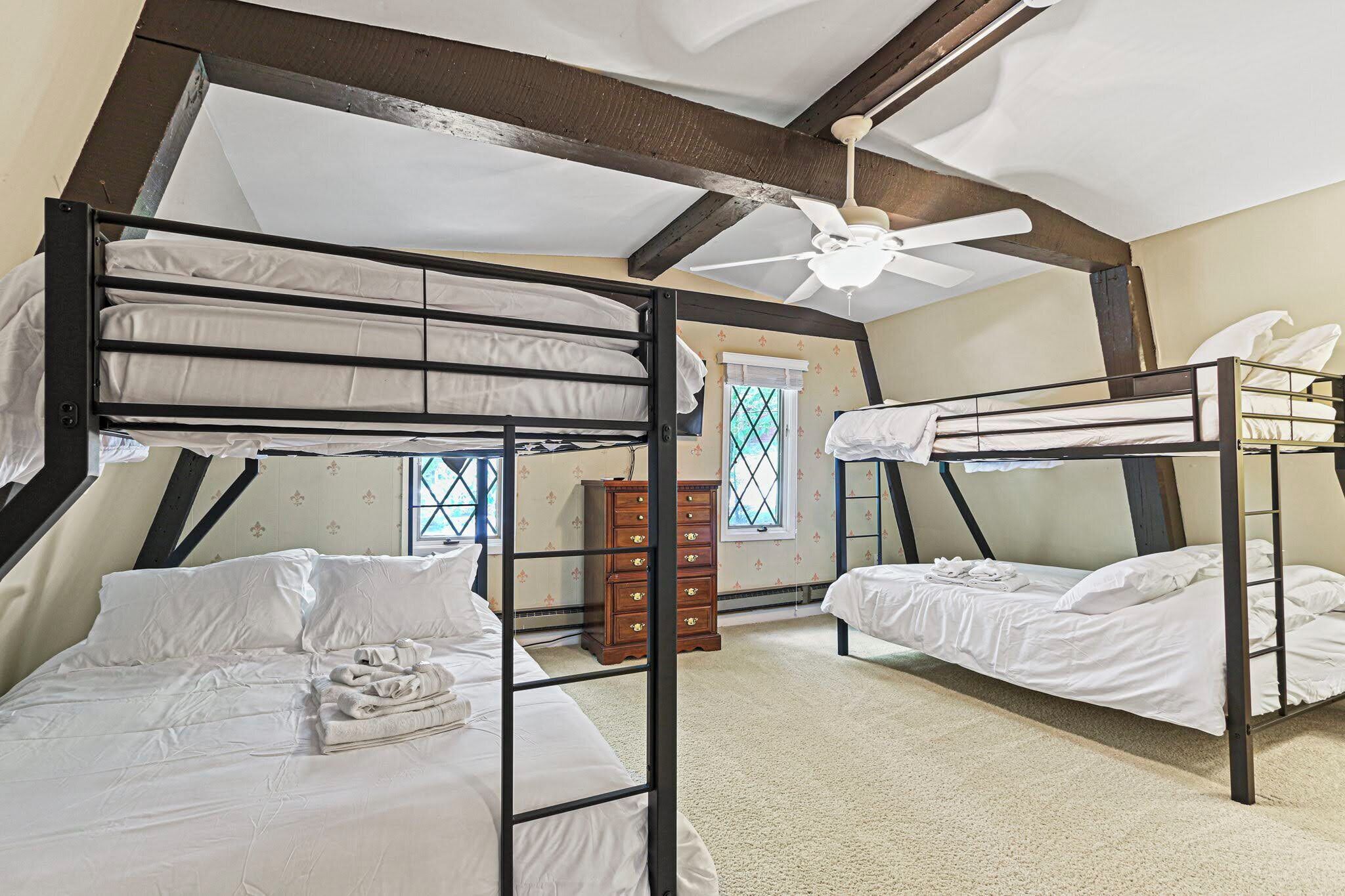 A dormitory room with bunk beds, a wooden dresser, and a ceiling fan.