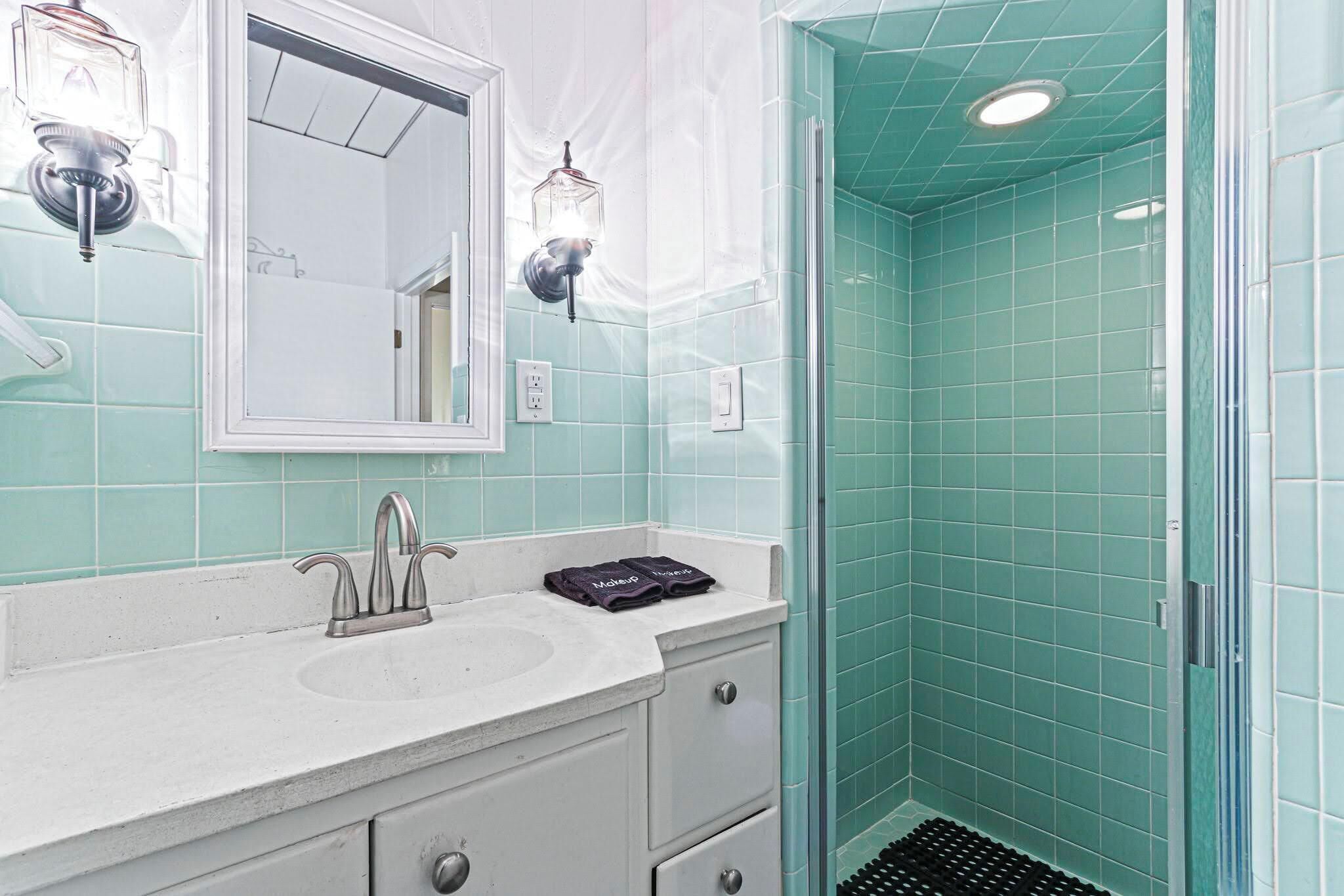 Een badkamer met een witte wastafel, een spiegel en een douche met blauwgroene tegels.
