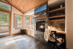 Ein modernes Wohnzimmer mit Kamin, Holzregalen und großen Fenstern.