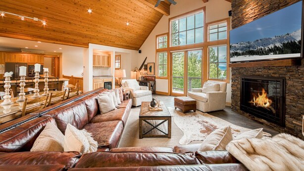 A spacious living room with a leather sofa, a fireplace, and large windows offering a view of the outdoors. - Easy Living at Northstar by Tahoe Getaways - 4BR Pet Friendly w/ Ski Shuttle & HOA (Truckee)