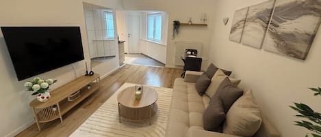 Un salon moderne doté d’un grand téléviseur à écran plat, d’un canapé beige, d’une table basse et d’un tapis à motifs.