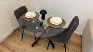 A round glass table with two black chairs, a glass wine glass, and two white plates on woven placemats. - Ground Serenity (Saint-Gilles)
