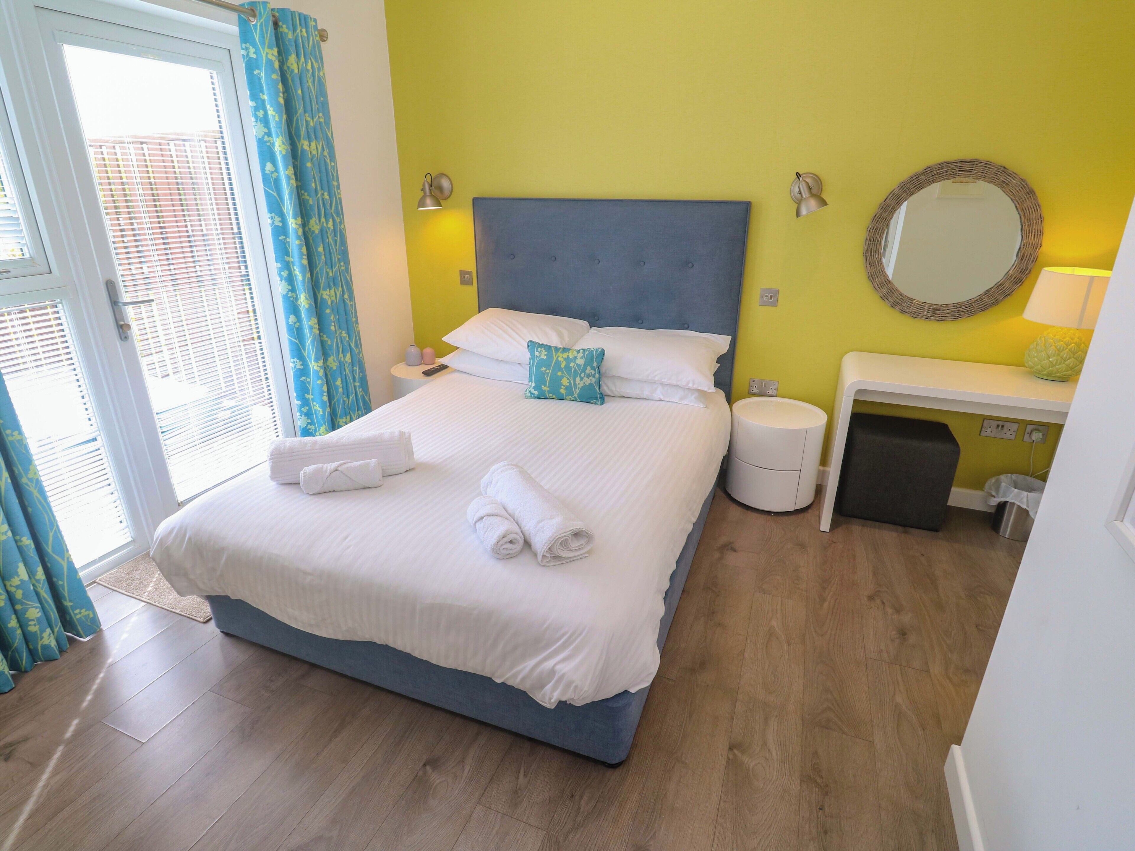 A hotel room with a bed, bedside tables, a mirror, and a window with curtains.