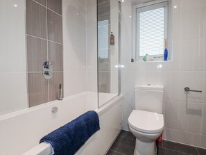 Ein modernes Badezimmer mit Badewanne, Toilette und einem Fenster mit Jalousien.