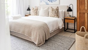 A bedroom with a large bed, a ceiling fan, a bedside table with a lamp, a wooden door, and a woven basket. - Winelands Mountain View Oasis - 3 Bedroom House, Gym, Pool, Cinema, Lounge, BBQ (Franschhoek)