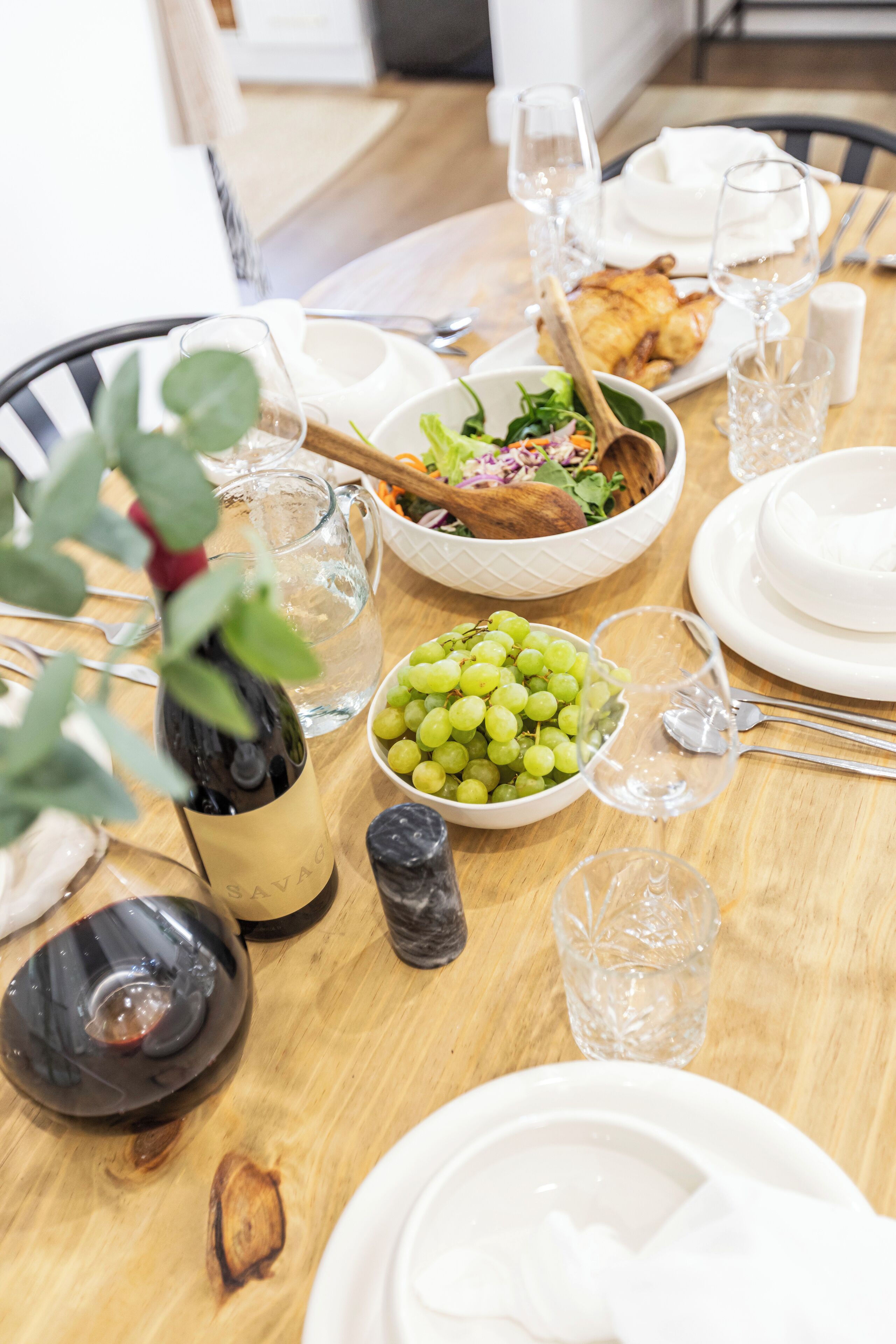 A dining table set with plates, bowls, glasses, and a bottle of wine.