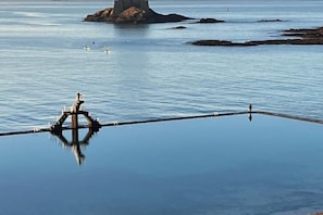 A calm body of water with a clear reflection of a structure, a small island with a tower, and a few people in the distance. - Quiet studio within the city walls, 150m from the beach (Saint-Malo)