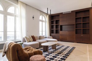 A modern living room with a sectional sofa, a round ottoman, a small table, and a large wooden shelving unit. - Stunning private hotel with rooftop terrace - Neuilly (Neuilly-sur-Seine)