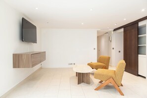 A modern living room with a flat-screen TV mounted on the wall, a wooden cabinet, a round coffee table, and two textured armchairs. - Stunning private hotel with rooftop terrace - Neuilly (Neuilly-sur-Seine)