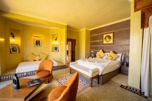 Quarto de hotel com duas camas, um espaço de estar com uma cadeira, uma mesinha e um detalhe decorativo na parede.