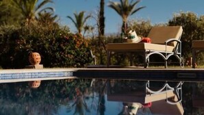 A poolside area with lounge chairs and a table, surrounded by palm trees and greenery. - Domaine Almaz 2 Villas and 3 Pools (Aghouatim)