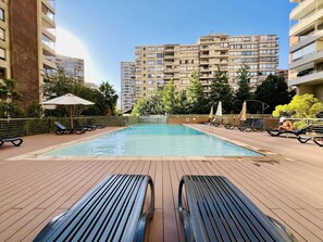 Ein Pool auf dem Dach mit Liegestühlen und Sonnenschirmen, umgeben von hohen Gebäuden.