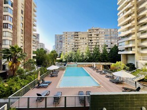 Ein Dachpool mit Liegestühlen und Sonnenschirmen, umgeben von Grünflächen und Hochhäusern.