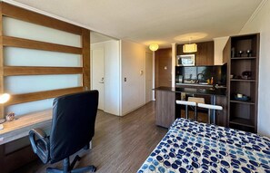 Quarto de hotel compacto com cama, escrivaninha, cadeira, cozinha compacta e um pequeno espaço de estar.