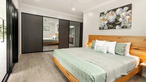 A bedroom with a large bed, a wooden headboard, a ceiling fan, and a painting on the wall. - Barron Heights in Caravonica (Cairns)
