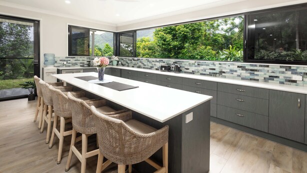 A modern kitchen with a large island, bar stools, and a view of greenery outside. - Barron Heights in Caravonica (Cairns)