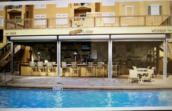 A poolside bar with outdoor seating, a pool, and a building with 'MEN' and 'WOMEN' signs. - 3Bd Resort 3 Miles to Disney (Orlando)