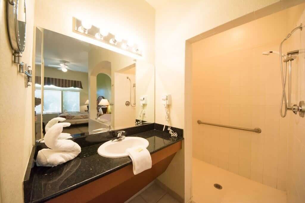 A bathroom with a black countertop sink, a mirror, and a shower area.