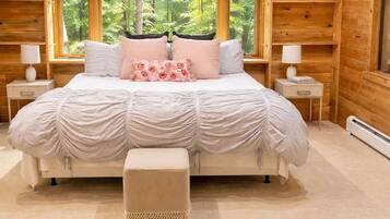 A bedroom with a large bed, two bedside tables, and a window with a view of trees.