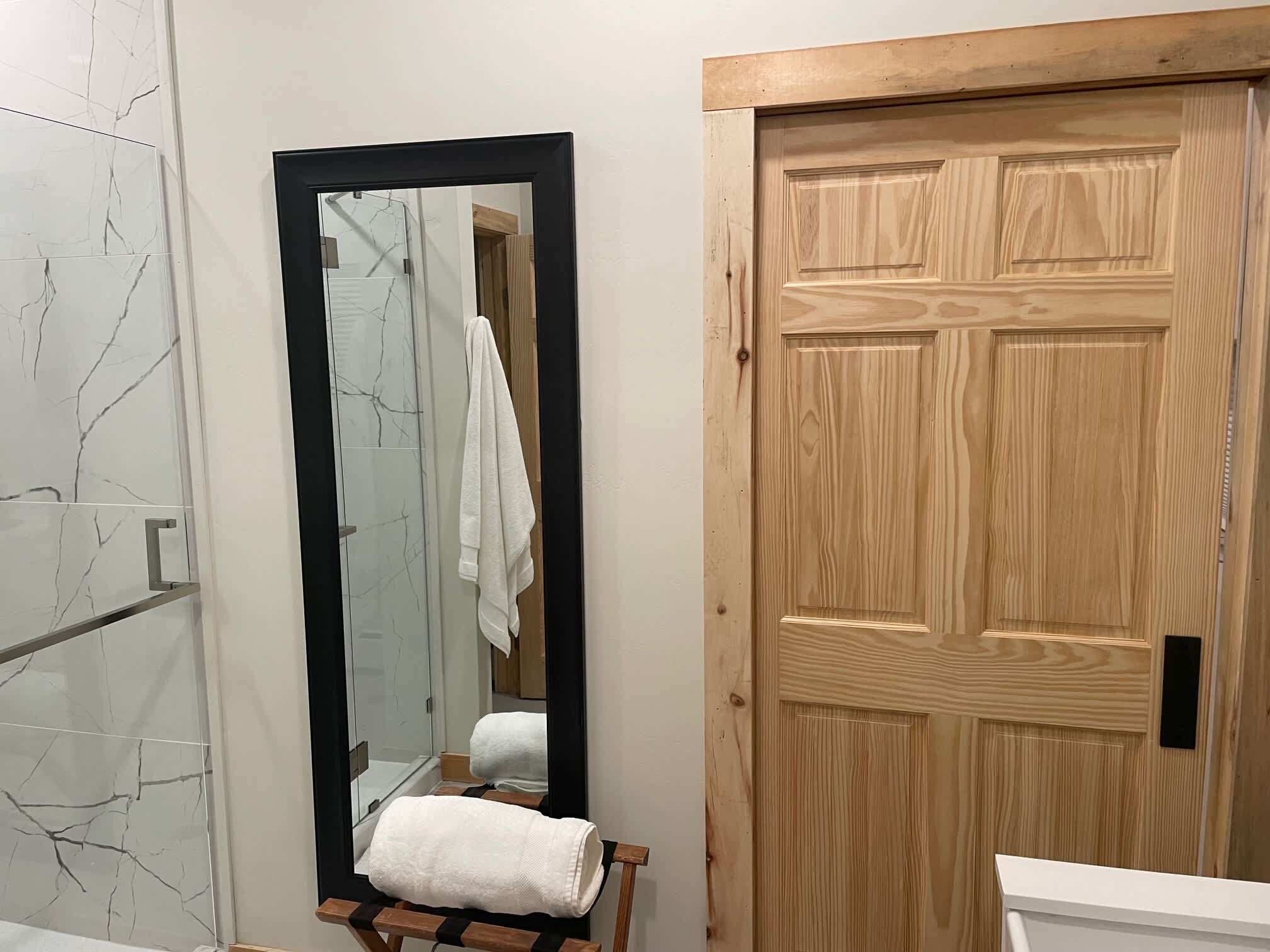A bathroom with a marble-tiled wall, a wooden door, a mirror, and a towel rack.