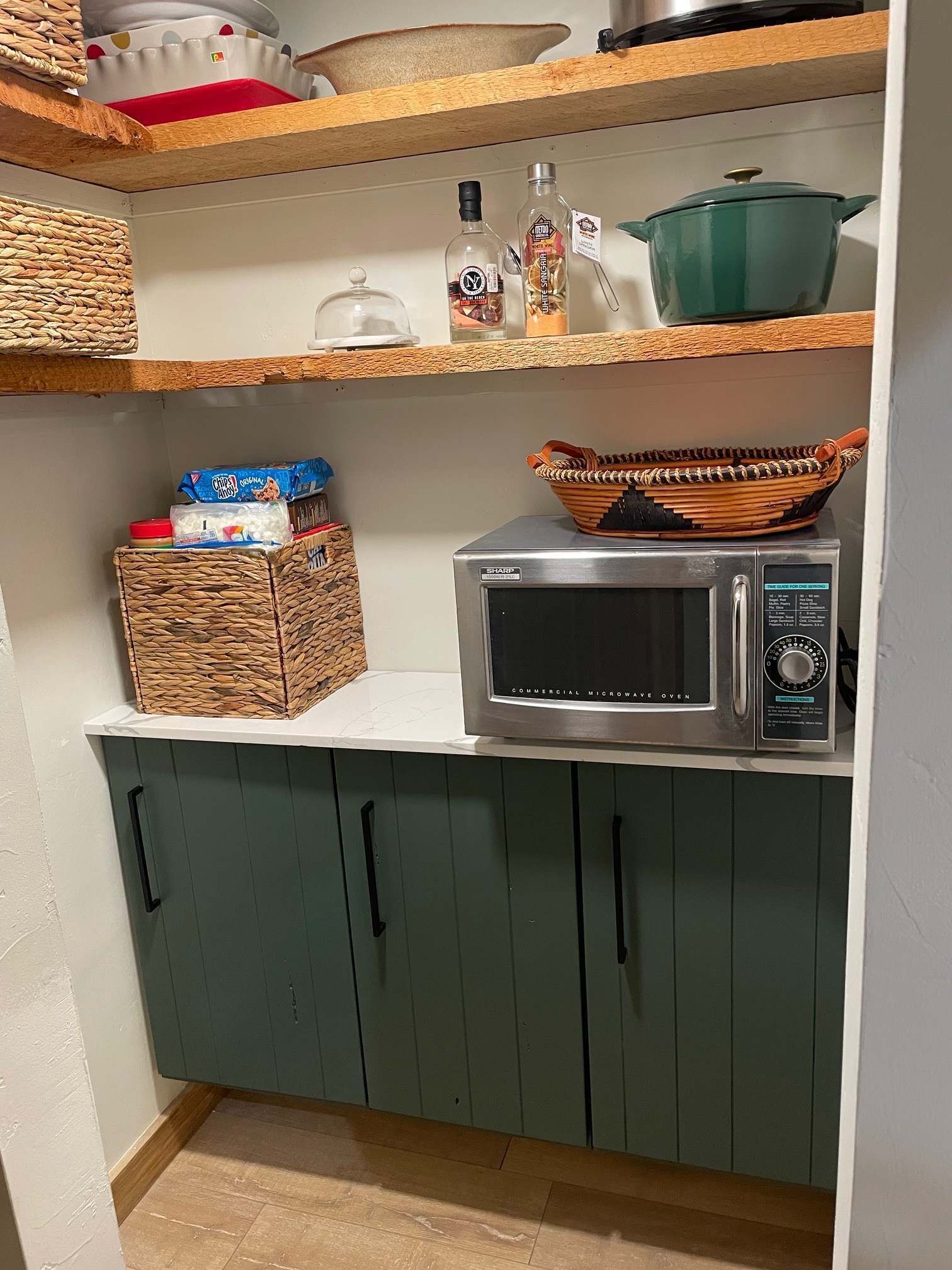 Uma cozinha com micro-ondas, cestos de vime e uma panela verde sobre a bancada.