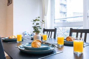 A breakfast setting with croissants, orange juice, and a vase with a plant on a table. - Spacious 2BR Flat - Bounds Green Private Parking (London)