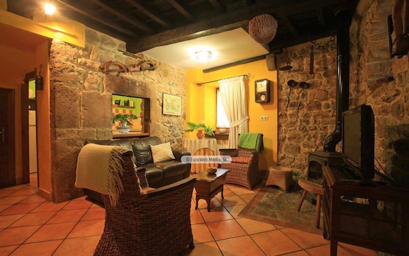 A cozy living room with a stone wall, a fireplace, a leather sofa, and a television.