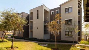 A modern apartment building with a flat roof, multiple balconies, and a well-maintained lawn with young trees. - The Steynview Apartment (Sandton)
