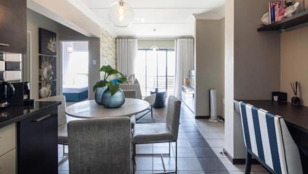 A modern kitchen with a dining area, featuring a round table, chairs, and a hanging light fixture. - The Steynview Apartment (Sandton)