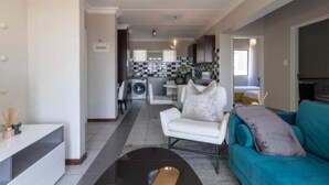A modern living room with a sofa, a coffee table, and a kitchen in the background. - The Steynview Apartment (Sandton)
