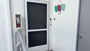 En hvid dør med glasrude, brandalarm, dørmåtte og ringeklokke.