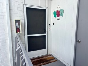 A white door with a glass panel, a fire alarm, a welcome mat, and a doorbell. - 1017 - Premium - Beach Front (Siesta Key)