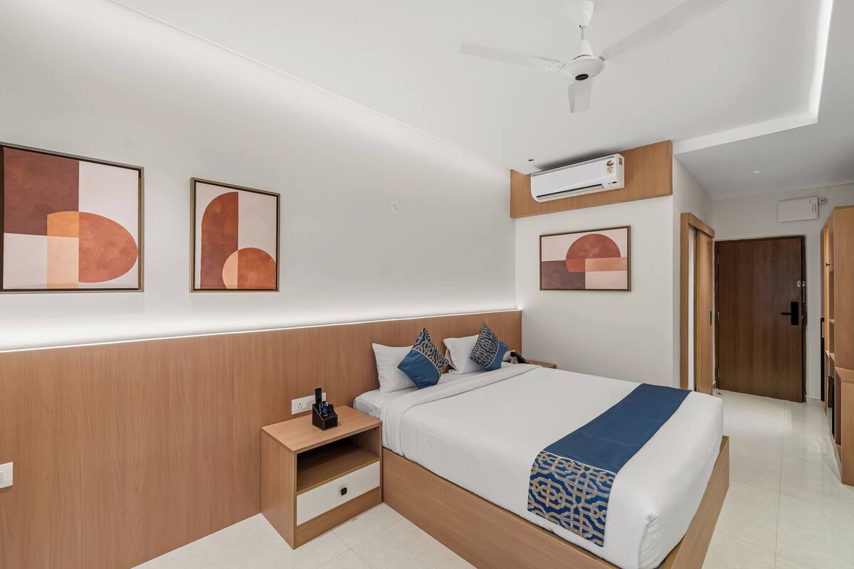 A modern hotel room with a large bed, bedside tables, a ceiling fan, and artwork on the walls.