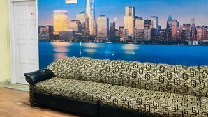 A room with a sofa facing a mural of a city skyline. - Roomshala Hotel Blue Inn Noida Sector 51 (Noida)