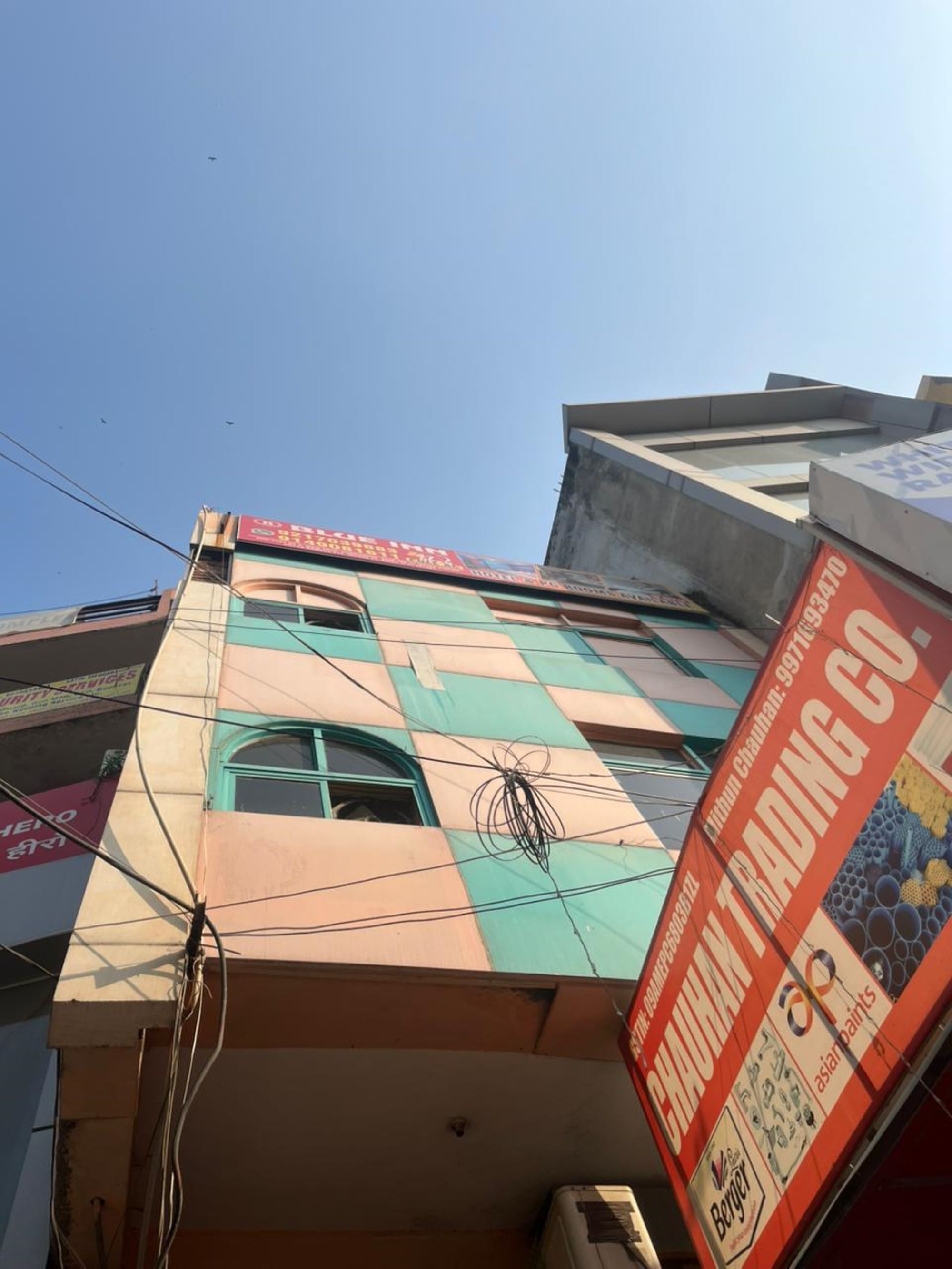 Un edificio de varios pisos con espacios comerciales y residenciales. Se observan carteles de una empresa comercial y un proveedor de servicios. El edificio tiene varias ventanas y una línea eléctrica visible.