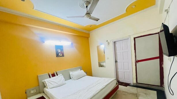 A bedroom with a bed, a ceiling fan, a door, and a wall-mounted TV. - Roomshala Hotel Blue Inn Noida Sector 51 (Noida)
