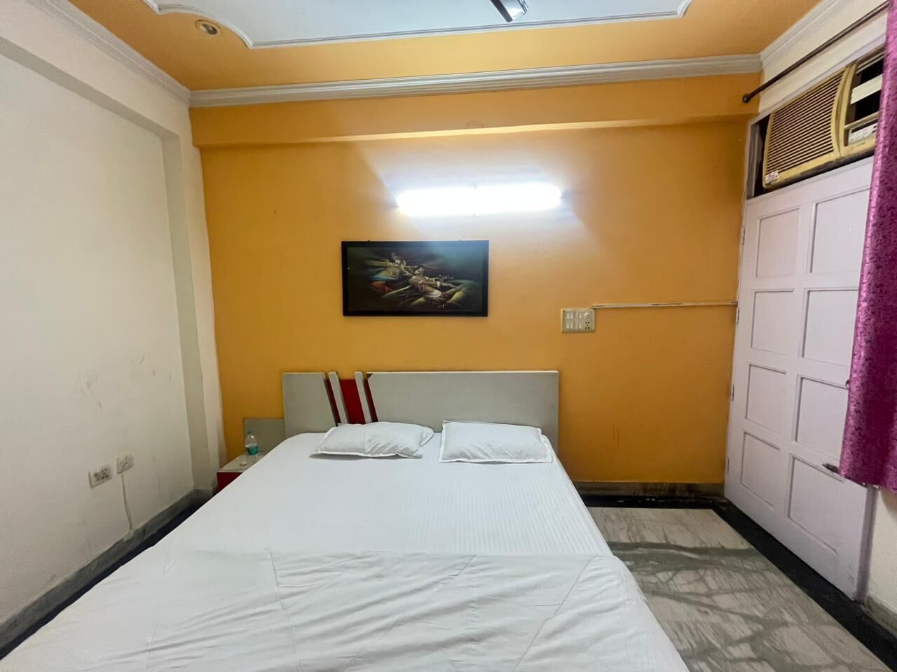 A bedroom with a bed, a painting on the wall, and a door with a purple curtain.