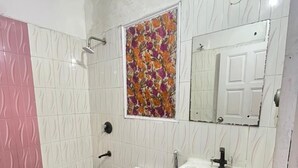 A bathroom with a toilet, sink, shower, and a decorative floral wall piece. - Roomshala Hotel Blue Inn Noida Sector 51 (Noida)