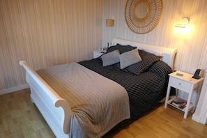 Un lit bien fait, avec une couvre-lit à rayures et des oreillers, une table de chevet avec une lampe et un luminaire fixé au mur.