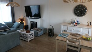 Una sala de estar moderna con un televisor de pantalla plana, una chimenea, un comedor con una mesa de madera y una zona de cocina con un reloj y varias botellas.
