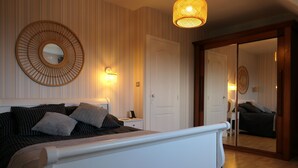 Un dormitorio con cama, mesita de noche, lámpara y un espejo en la pared.