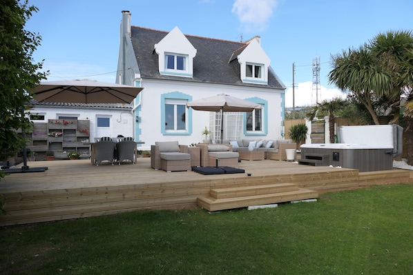 Une maison avec une terrasse, du mobilier d’extérieur et un jacuzzi.